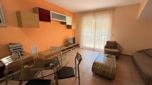 Uma sala de estar moderna com uma mesa de jantar de vidro, cadeiras, um sofá e uma TV em um suporte.