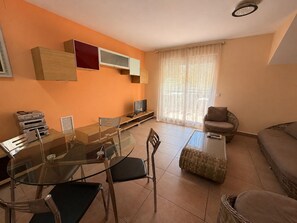 A modern living room with a glass dining table, chairs, a sofa, and a TV on a stand. - Delfines III bl.IV esc.3 2º Solo Familias! (Playa Xeraco)
