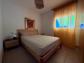 A bedroom with a bed, nightstand, lamp, and a painting on the wall. - Delfines III bl.IV esc.3 2º Solo Familias! (Playa Xeraco)
