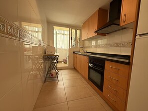 A kitchen with a microwave, oven, and wooden cabinets. - Delfines III bl.IV esc.3 2º Solo Familias! (Playa Xeraco)