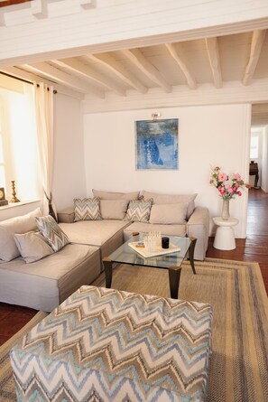 Ein Wohnzimmer mit einem Ecksofa, einem Glastisch und einem gemusterten Pouf.