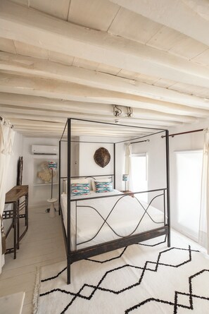 Ein Bett mit Baldachin, mit weißer Matratze und schwarzem Metallgestell, ein runder Spiegel an der Wand und ein Teppich mit geometrischem Muster auf dem Boden.