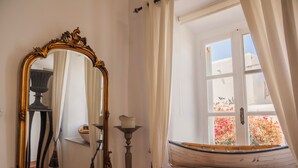 Een kamer met een grote, versierde spiegel, een raam met uitzicht op bloemen en een klein bootje.