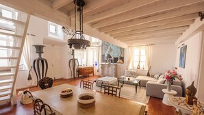 Een ruime woonkamer met een eethoek, houten balken in het plafond, een kroonluchter en een schilderij aan de muur.