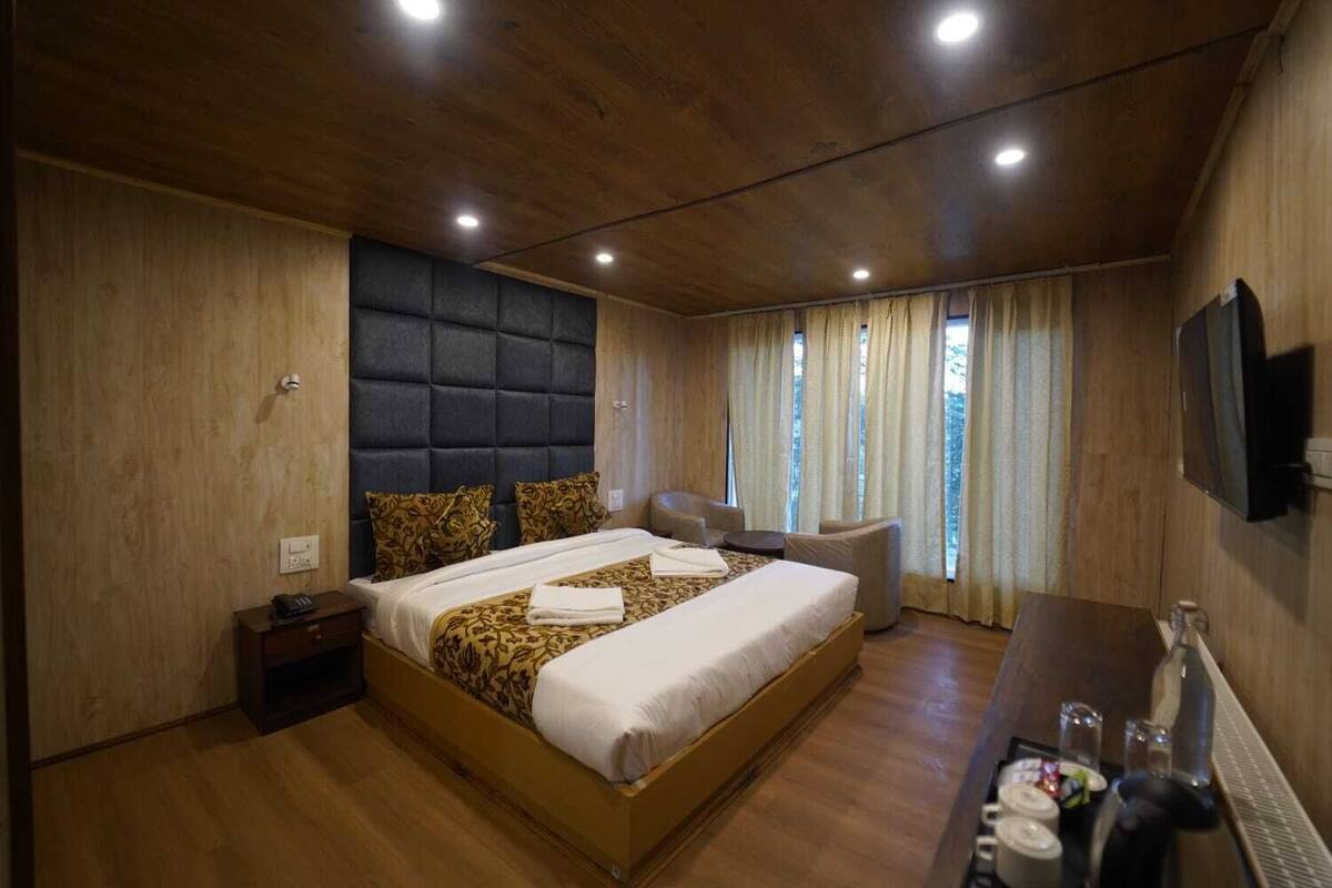 Quarto com uma cama grande, mesa de cabeceira, cadeira, televisão e janela com cortinas.