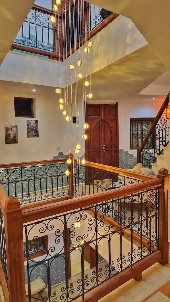 A multi-level interior with a wooden staircase, wrought iron railings, and hanging light fixtures. - Dar Almassir (Chefchaouen)