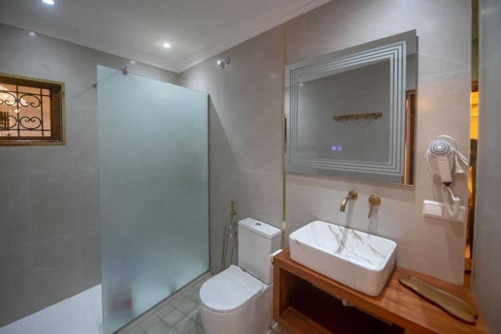 Une salle de bain avec une douche à parois de verre, des toilettes, un lavabo avec un miroir et un sèche-cheveux fixé au mur.