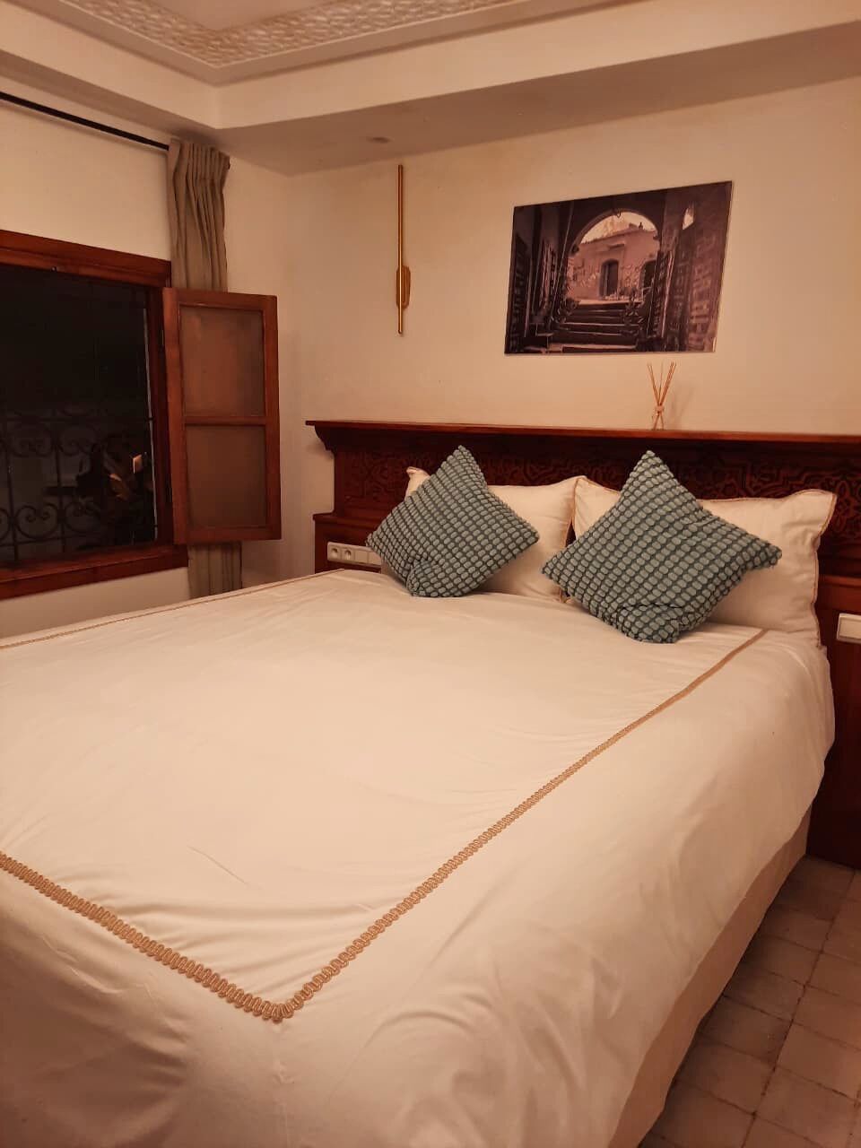 A neatly made bed with a wooden headboard, two patterned pillows, and a framed picture on the wall.