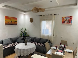 A living room with a sofa, a dining table set for four, and two paintings on the walls.