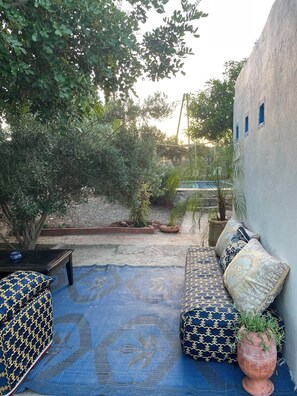 A covered outdoor seating area with a patterned rug, cushions, and a potted plant. - Dar Christelle villa 4 persons In the countryside (Ounagha)