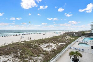 Blick auf einen Strand mit Poolbereich, Strandstühlen und einem Rettungsschwimmturm.