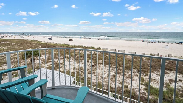 Un balcon donnant sur une plage, avec une balustrade blanche et quelques chaises.