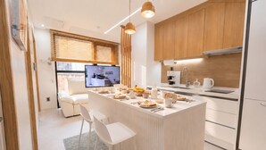 Eine moderne Küche mit einer zentralen Kochinsel, weißen Barhocker, Holzschränken und einem Essbereich mit einer Couch.