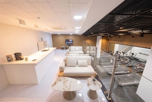 Un moderno vestíbulo de hotel con una recepción, zona de estar y equipo de ejercicio.