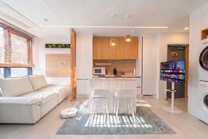 Une cuisine moderne dotée d’un îlot central, de tabourets de bar, d’un lave-linge et d’un téléviseur.