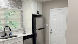 A kitchen with white cabinets, a stainless steel refrigerator, a sink with a faucet, and a window with blinds. - Welcome to Sandtown Villa—your home away from home. (Atlanta)