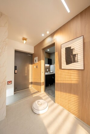 A modern hotel hallway with a robotic vacuum cleaner, a framed artwork, and a wooden wall. - PRANA I  Full-Service APT in Gangnam 5 min. Metro (SEOUL)