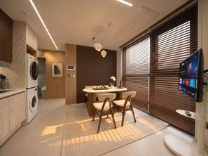 A modern kitchen with a built-in washer, a dining area with a round table and chairs, and a large TV mounted on the wall. - PRANA I  Full-Service APT in Gangnam 5 min. Metro (SEOUL)