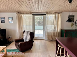 A living room with a brown leather armchair, a wooden coffee table, a green cabinet, and a sliding glass door leading to an outdoor deck. - 4 Star Holiday Home in Oro (Orø)