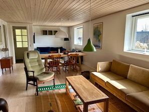 A living room with a wooden ceiling, a dining table with chairs, a sofa, a coffee table, and a green pendant light. - 4 Star Holiday Home in Oro (Orø)