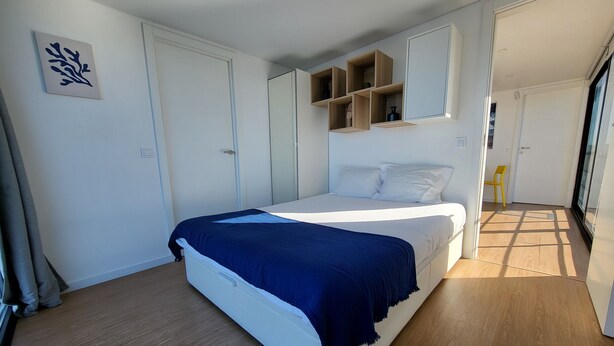 Ein Schlafzimmer mit einem Bett, einem Kleiderschrank, einem Spiegel und einer Tür zu einem anderen Raum.