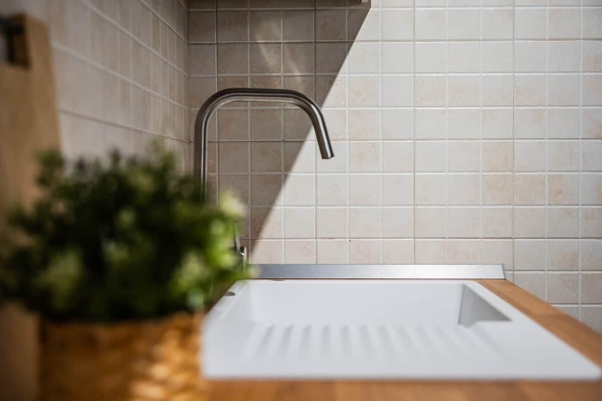 Een moderne keuken met een roestvrijstalen spoelbak, witte tegels en een houten aanrecht.