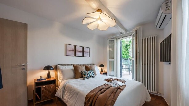 A bedroom with a bed, bedside tables, a ceiling light fixture, a window, and an air conditioning unit. - [Centro Storico] A/C, Terrazzo privato, WiFi (Fiorano Modenese)