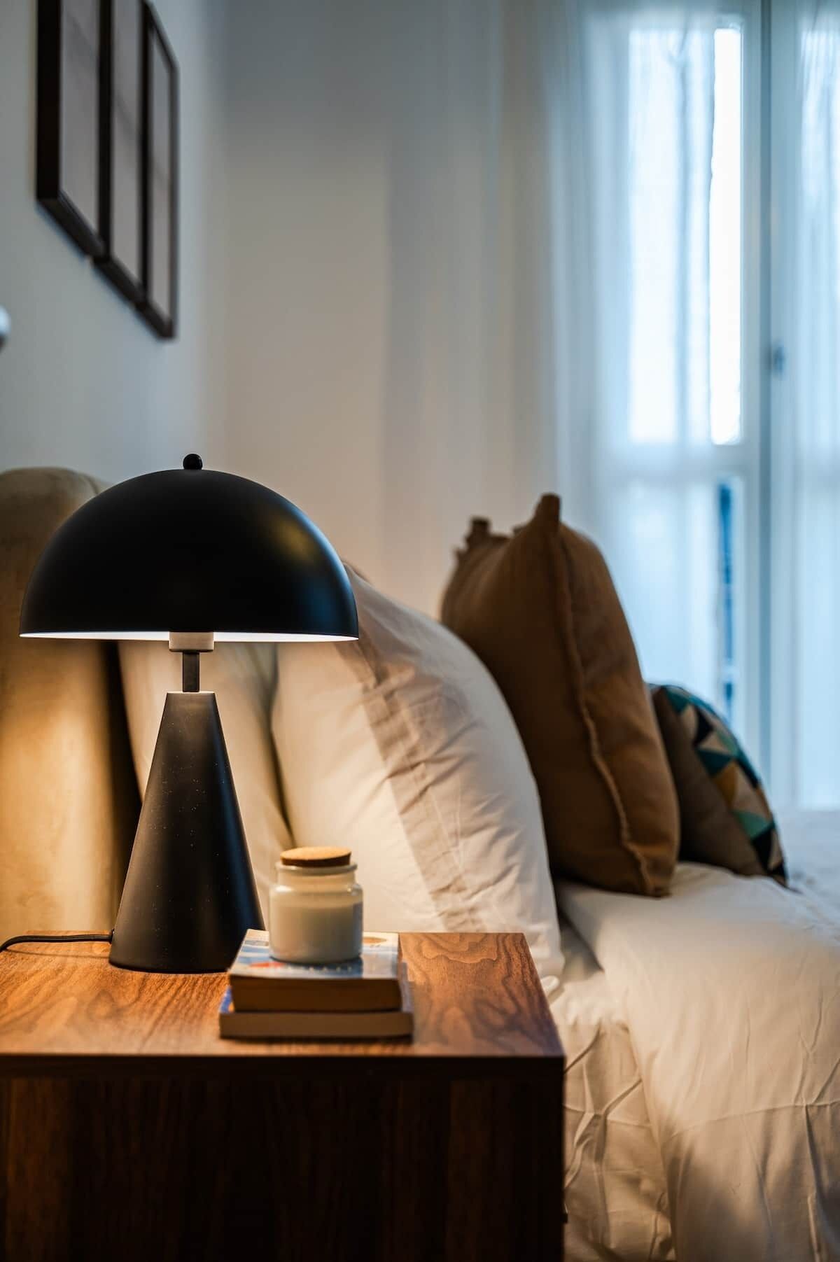 Une chambre à coucher avec une table de chevet, une lampe, un livre, un pot et un lit avec des oreillers.