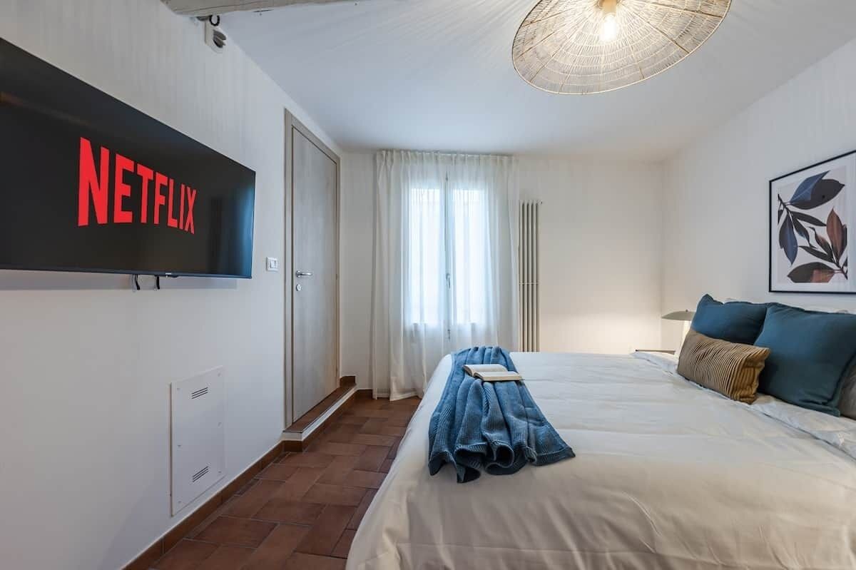A hotel room with a bed, a TV mounted on the wall, a door, and a window with curtains.