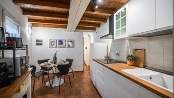 A compact kitchen with a wooden ceiling, white cabinets, a sink, and a dining area with chairs and a table.