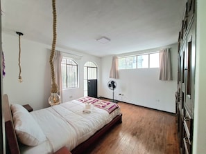 A bedroom with a bed, a fan, a window, and a door.