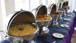 Ein Buffet mit mehreren Speiseauslagen, ein Tisch mit Geschirr und Besteck sowie ein Fenster mit Blick nach draußen.