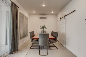 Uma área de refeições com mesa, cadeiras, planta e porta deslizante.