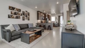 A modern living room with a grey sofa, a coffee table, and a TV mounted on the wall. - The Lofts #17 Townhome Pool Resort, Poolside and Hot tub (St. George)