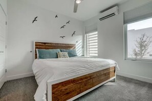 Quarto com cabeceira de madeira, cama com roupa de cama branca, janela com persianas e adesivos de pássaros na parede.
