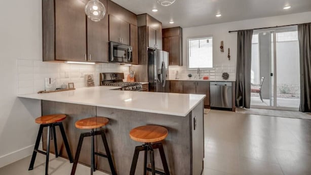 A modern kitchen with a large island, bar stools, stainless steel appliances, and pendant lighting. - The Lofts #17 Townhome Pool Resort, Poolside and Hot tub (St. George)