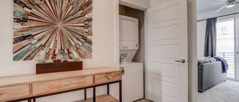 A room with a wooden console table, a wall-mounted abstract art piece, a white door, and a grey sofa in the background.