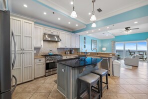 A modern kitchen with white cabinetry, a central island, stainless steel appliances, and a view to the outside. - Escapes to the Shores Penthouse 1802 by Liquid Life (Orange Beach)