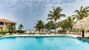 A clear blue pool with lounge chairs, palm trees, and a building with a red roof. - Private 2BR 3RD Floor Villa-Shared Pool-Beach (North Placencia)