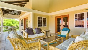 A covered outdoor seating area with wicker furniture, a glass-top table, and a view of greenery. - Private 2BR 3RD Floor Villa-Shared Pool-Beach (North Placencia)