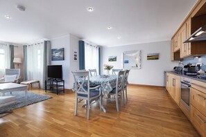 Eine moderne Küche mit Holzschränken, ein Essbereich mit Tisch und Stühlen sowie ein Fernseher.
