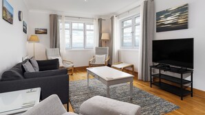 Un salon moderne avec un canapé, un fauteuil, une table basse, un téléviseur et des œuvres d’art accrochées au mur.