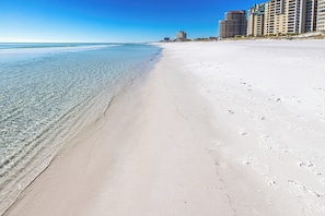 Ein Strand mit klarem Wasser, einem weiten Sandufer und Hochhäusern im Hintergrund.