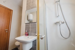 A bathroom with a white sink, a toilet, a shower with a handheld showerhead, and a wooden door. - Bright 1-bedroom apartment in central Sliema, steps from the seafront and Balluta Bay. Air conditioning, free Wi-Fi, fully equipped kitchen. Perfect base to explore Malta. (Sliema)