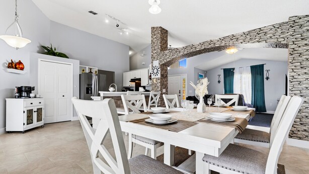 A modern kitchen with white cabinets, a stone accent wall, and a dining area with white furniture. - Lake Serenity Retreat Private Pool, Lake Views, Game Room & Outdoor TV (Kissimmee)