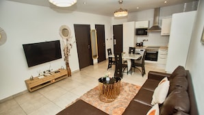 A modern living room with a flat-screen TV, a sofa, a coffee table, and a dining area with chairs and a table. - Cozy 1-bedroom apartment in SIGNATURE (Accra)