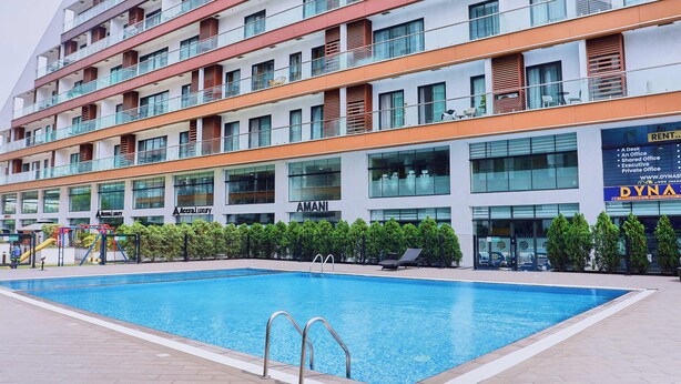 A modern hotel with a swimming pool, multiple balconies, and a sign for 'Dynasty' on the right. - Cozy 1-bedroom apartment in SIGNATURE (Accra)