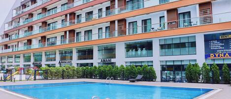 Un hotel moderno con piscina, varios balcones y un cartel que dice 'Dynasty' a la derecha.
