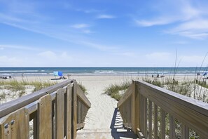 Ein hölzerner Steg führt zu einem Sandstrand mit Blick auf das Meer.