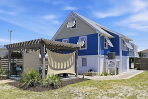 Ein zweistöckiges Haus mit blauer Fassade, einer Holzpergola und einem kleinen Garten.